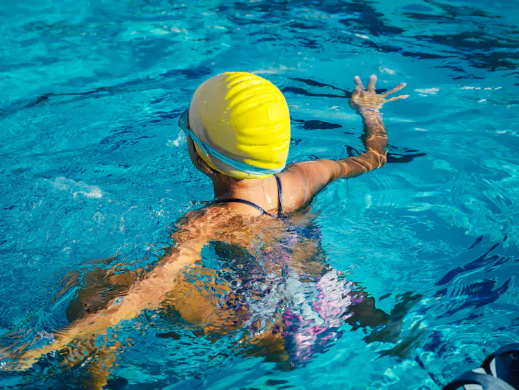 A swimmer with a yellow cap in the pool seen from the back.