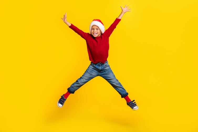 An excited kid in a Santa hat, jumping in the air.