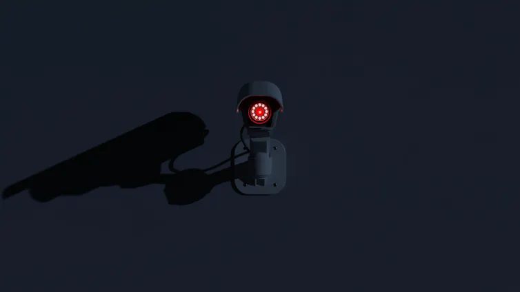 Surveillance camera with red lens glowing in the dark.