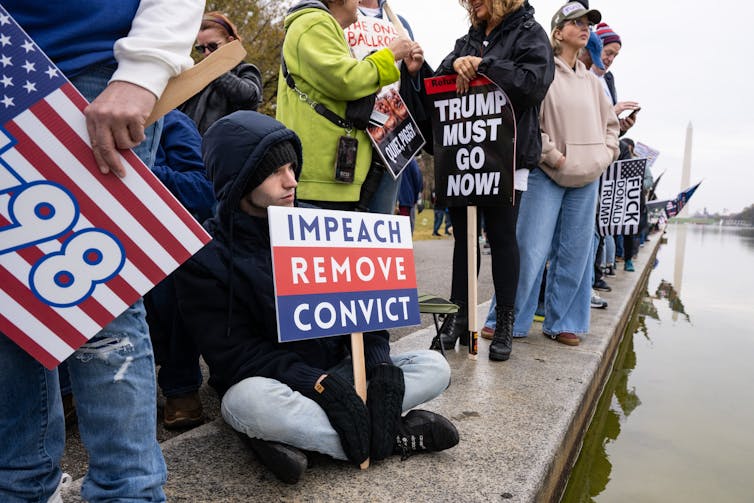 A protester holding a sign that reads 'impeach, remove, convict'.