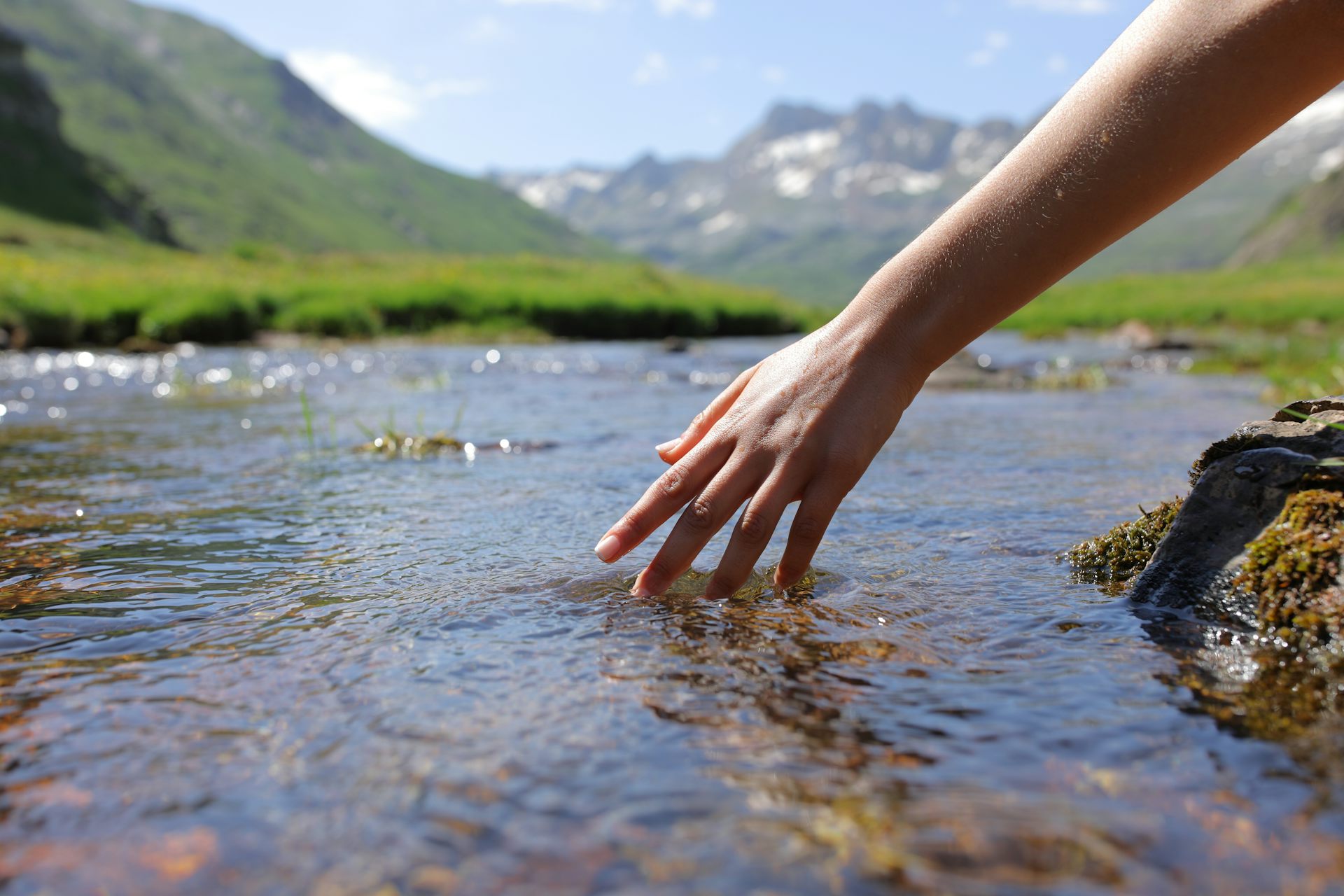 Person trails hand in stream with hills in the background.