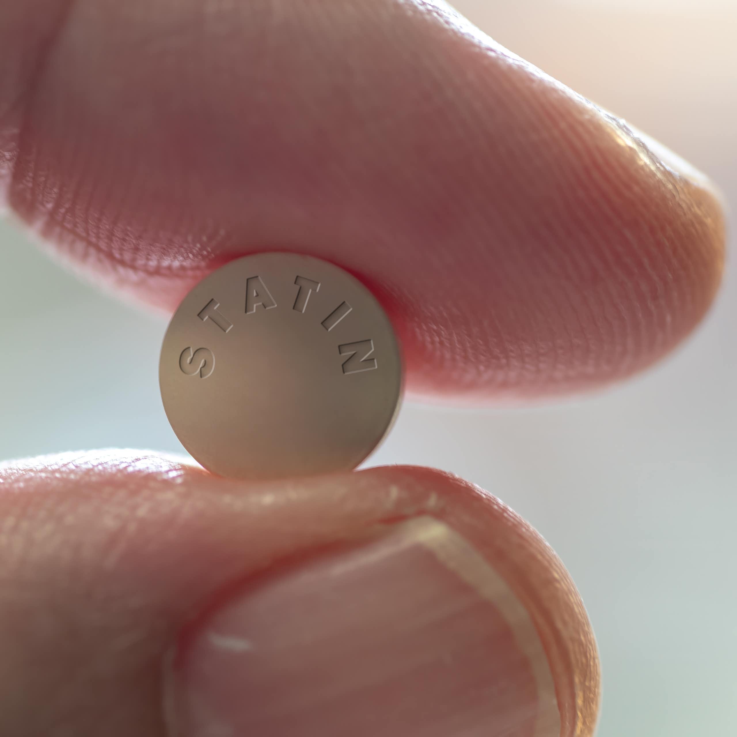 Fingers holding statin drug tablet - close up