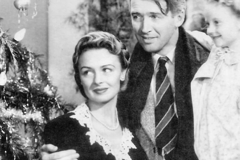 A man with his arms around a woman holding a child in a nightgown next to a Christmas tree.