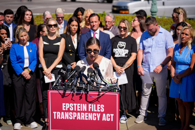 A woman speaks at a lectern with a sign on it that says "Epstein Files Transparency Act"