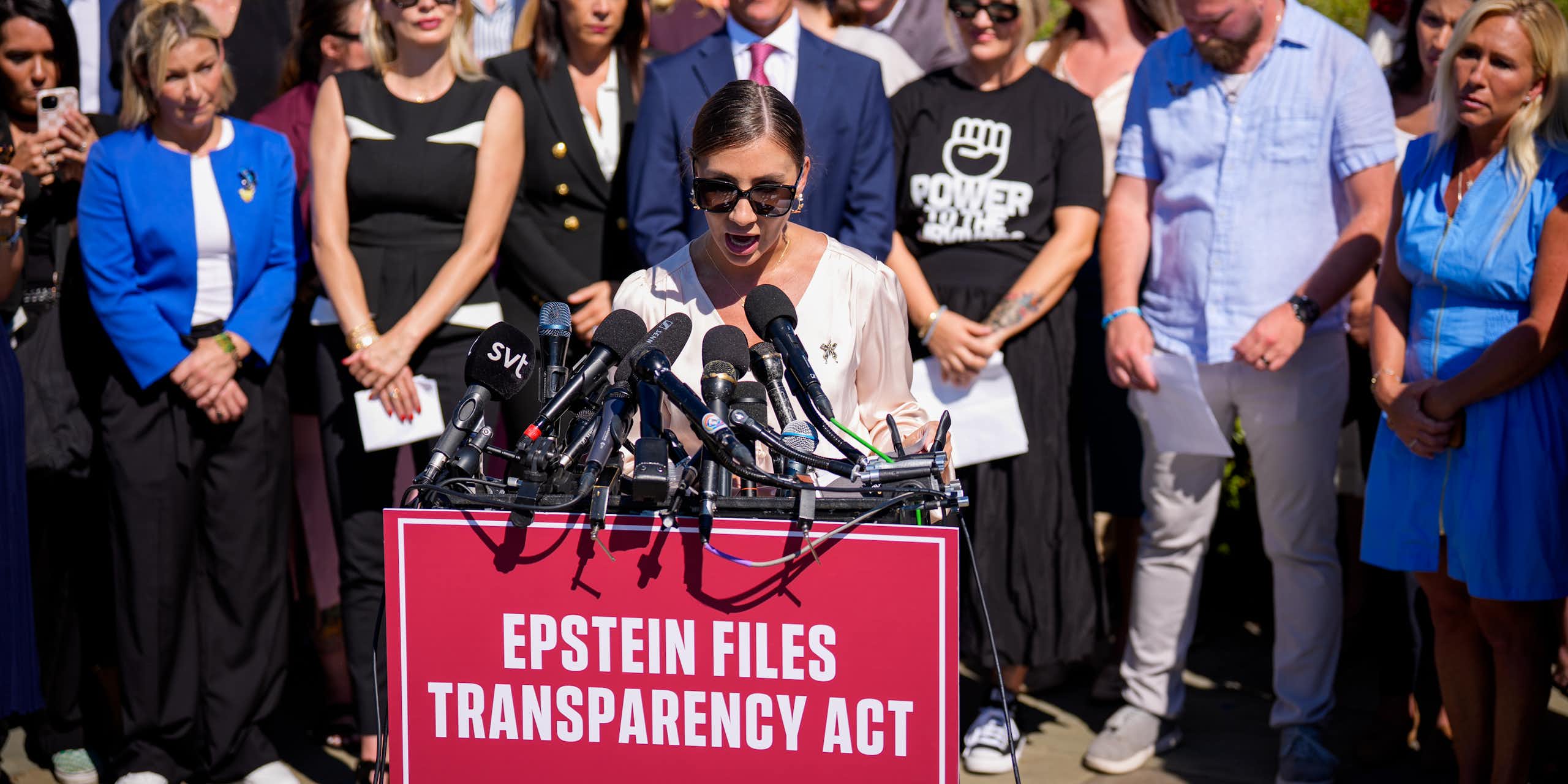 A woman speaks at a lectern with a sign on it that says "Epstein Files Transparency Act"