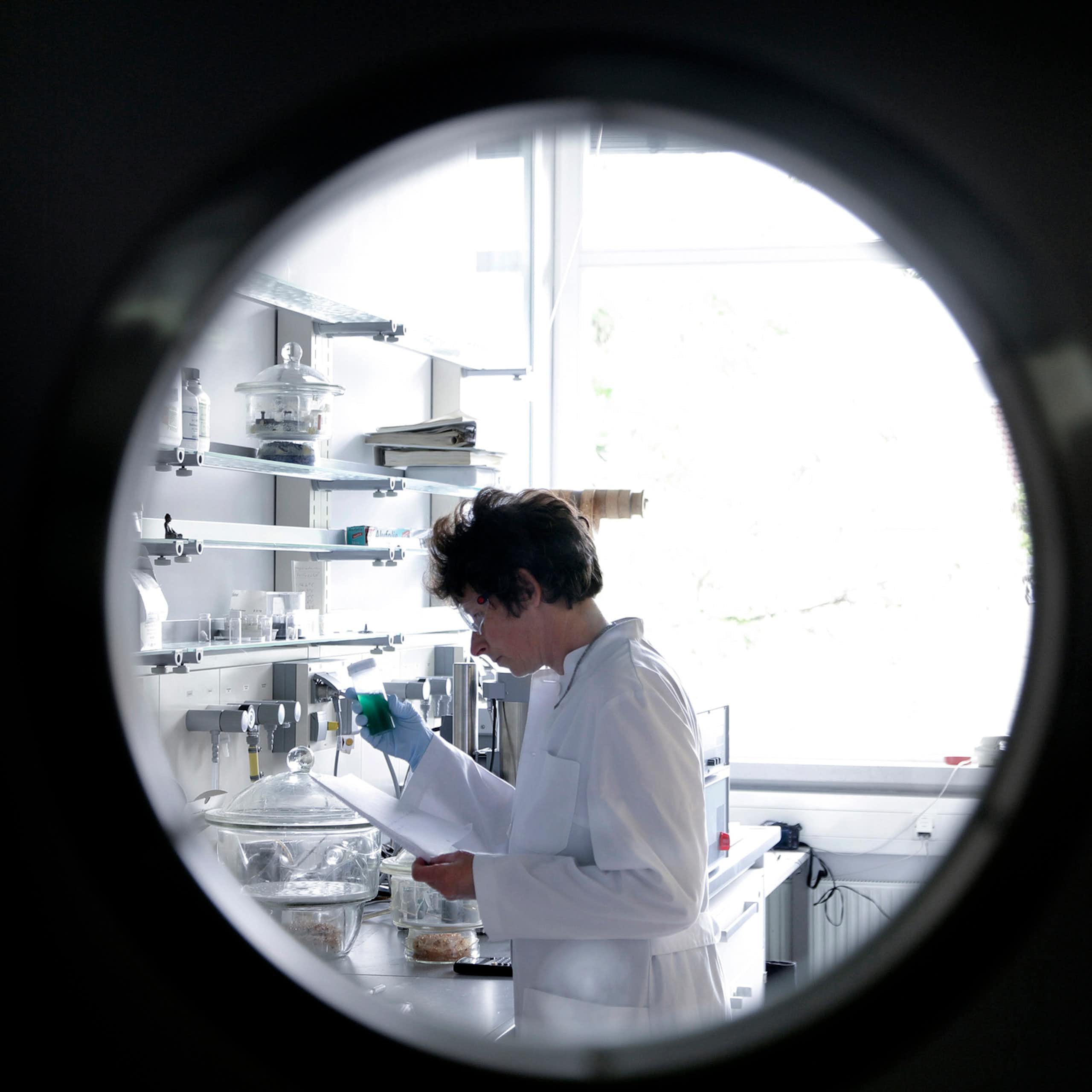 A porthole view of a scientist in a white coat in a lab.