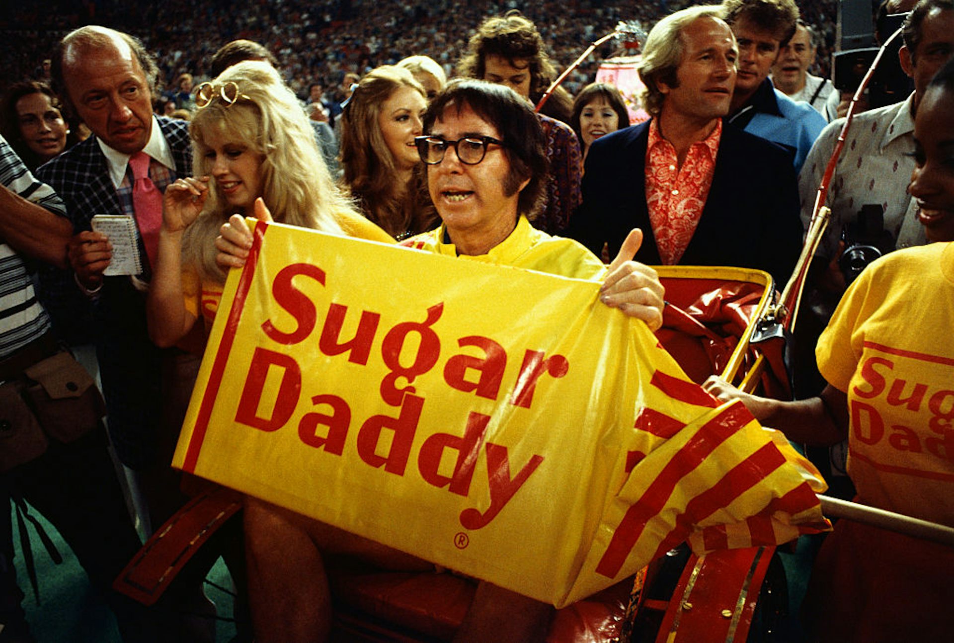 Man wearing glasses holds a yellow sign reading 'Sugar Daddy.'