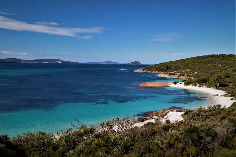 A calm, turqoise bay ringed by white sand and bushland.