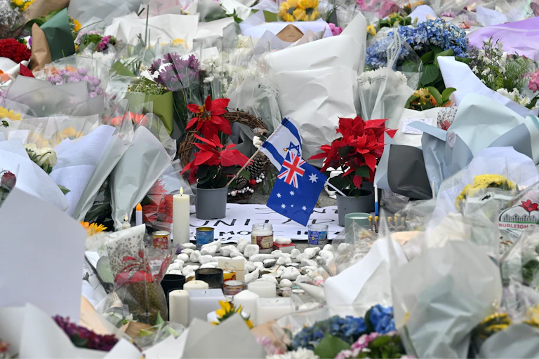 A memorial of a heap of bunches of flowers on the ground around small Israeli and Australian flags