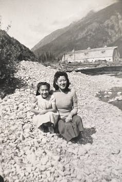 a smiling asian woman with her arm around a young girl with mountains in the background