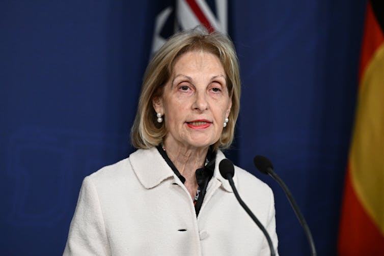A woman with a blonde bob speaks at a lectern