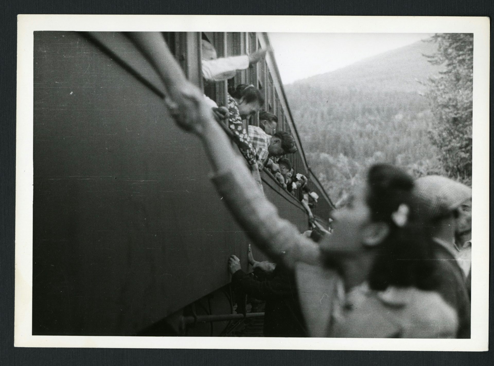 An Asian woman reaches up to clasp the hand of an unseen person on a train.