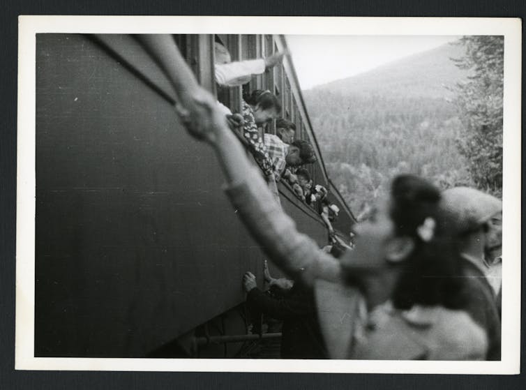 An Asian woman reaches up to clasp the hand of an unseen person on a train.