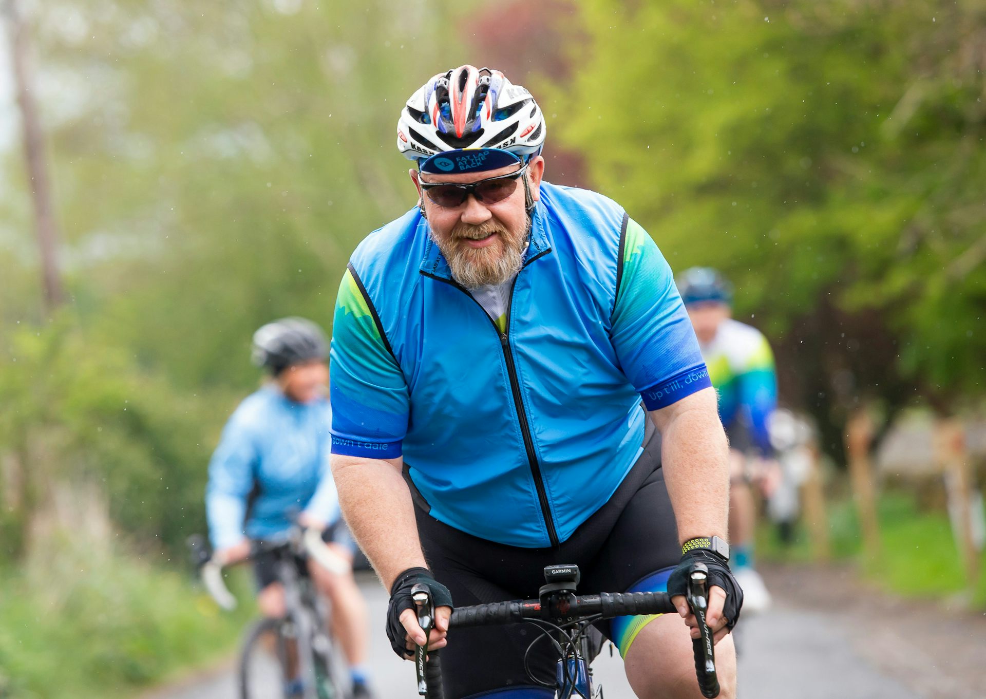 A man with a gray beard riding a motorcycle in a blue jersey