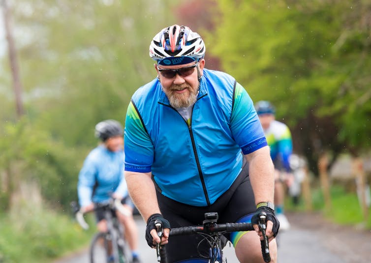 A man with a gray beard riding a motorcycle in a blue jersey