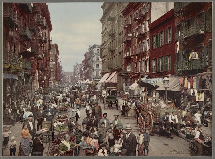 A colourised photo of a crowded street with vegetable stalls.