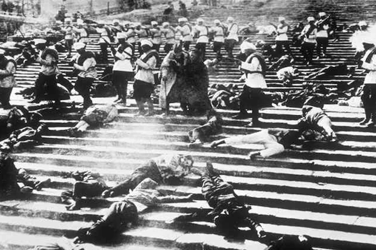 A wide film shot of a group of citizens shot down on public steps.
