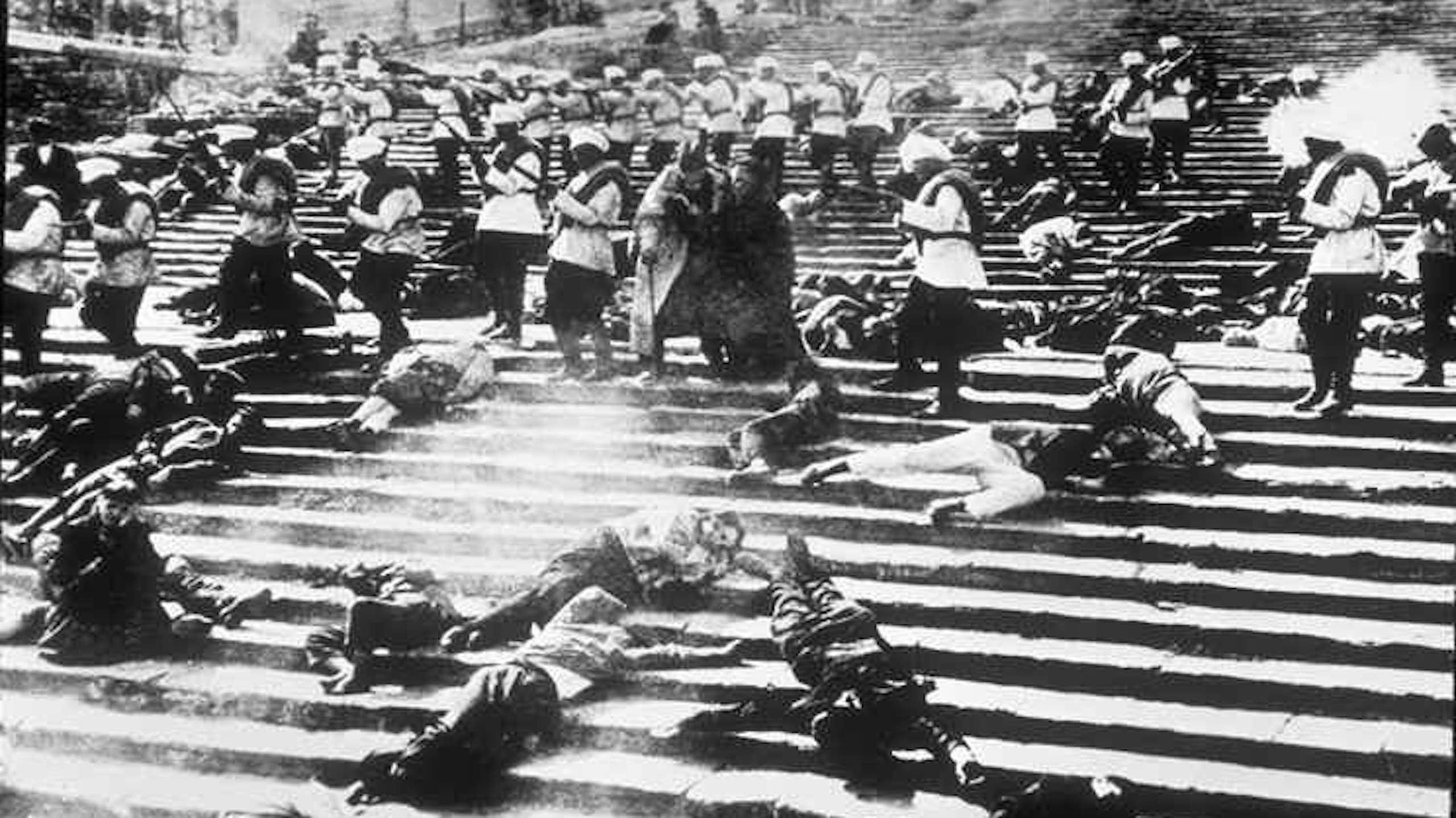 A wide film shot of a group of citizens shot down on public steps.