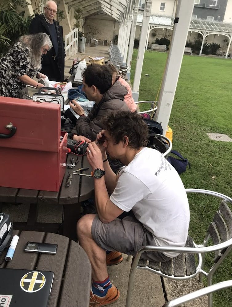 Stuart Walker (in white shirt) sitting at a table helping people repair items.