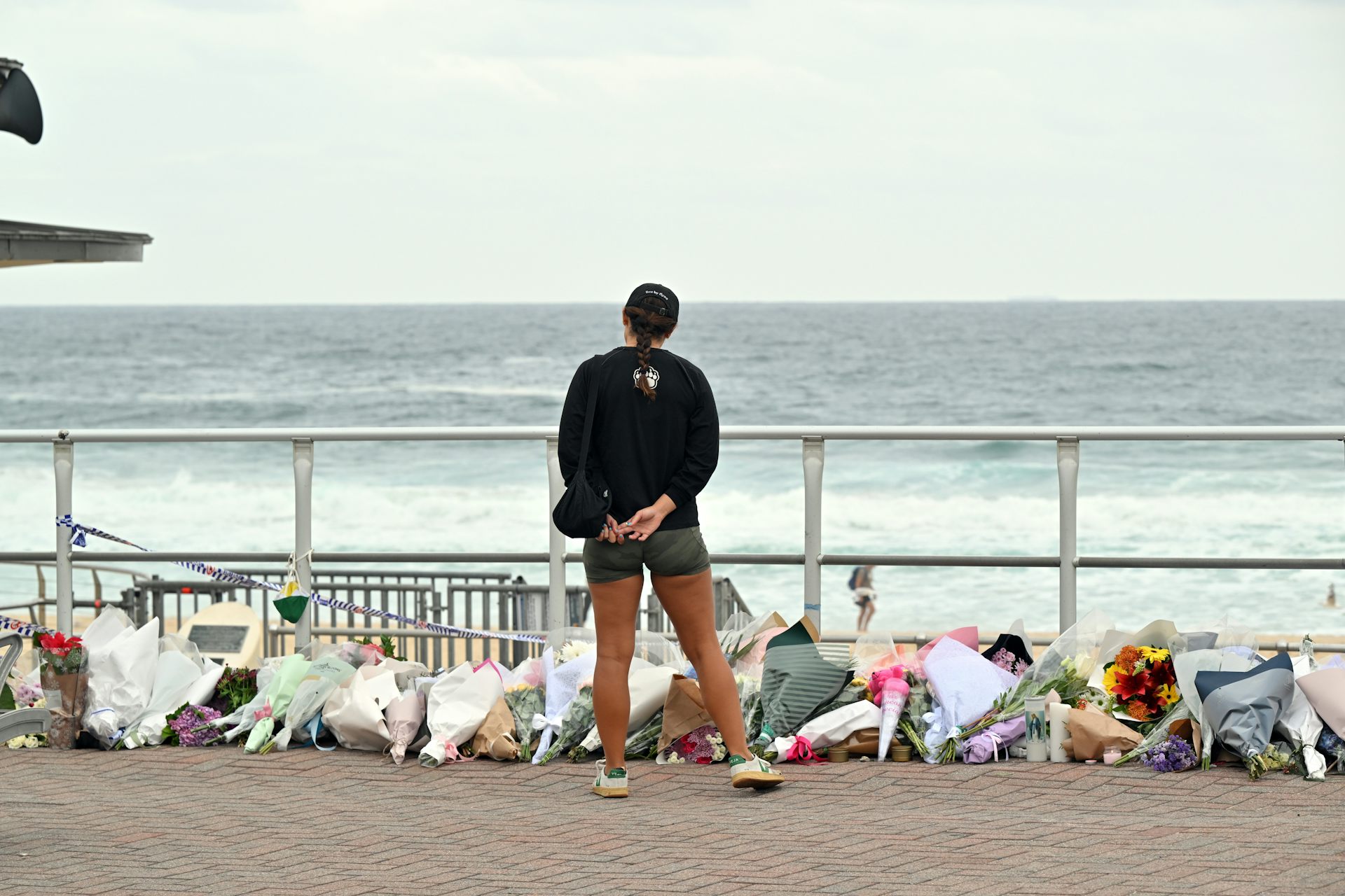 View from behind of a woman looking at a pile of flowers with the ocean in the background.