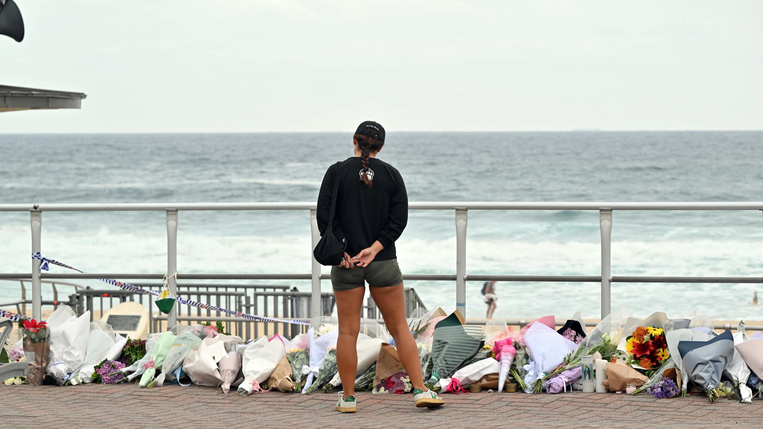 View from behind of a woman looking at a pile of flowers with the ocean in the background.