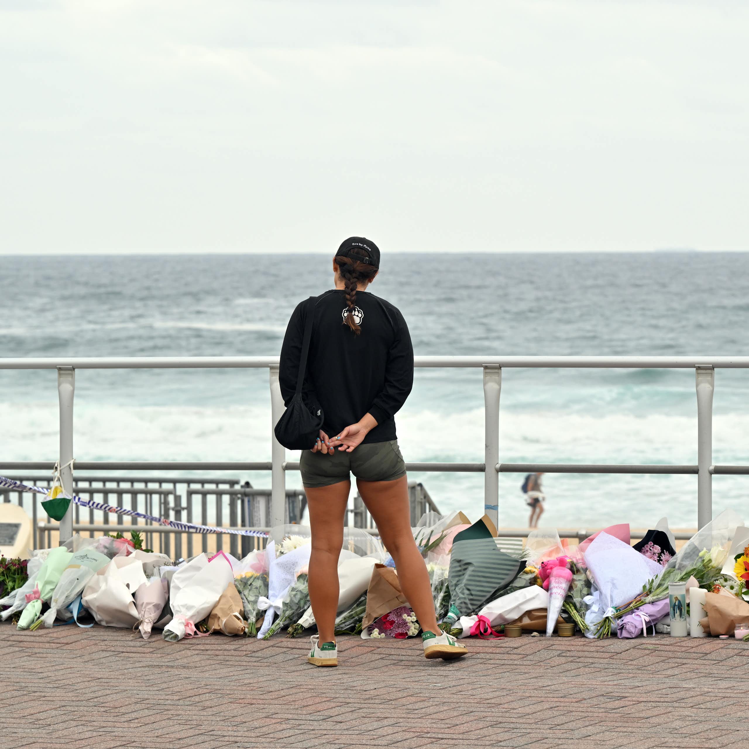 View from behind of a woman looking at a pile of flowers with the ocean in the background.