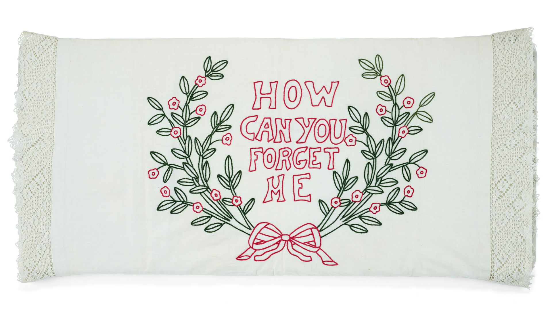A white pillowcase with embroidery depicting a bow, green plants and the text 'How Can You Forget Me.'