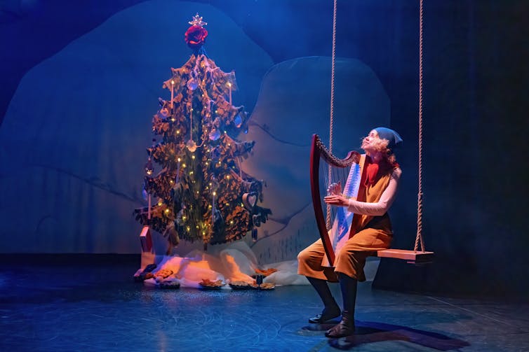 A young girl dressed as a Moomin character strumming a harp.