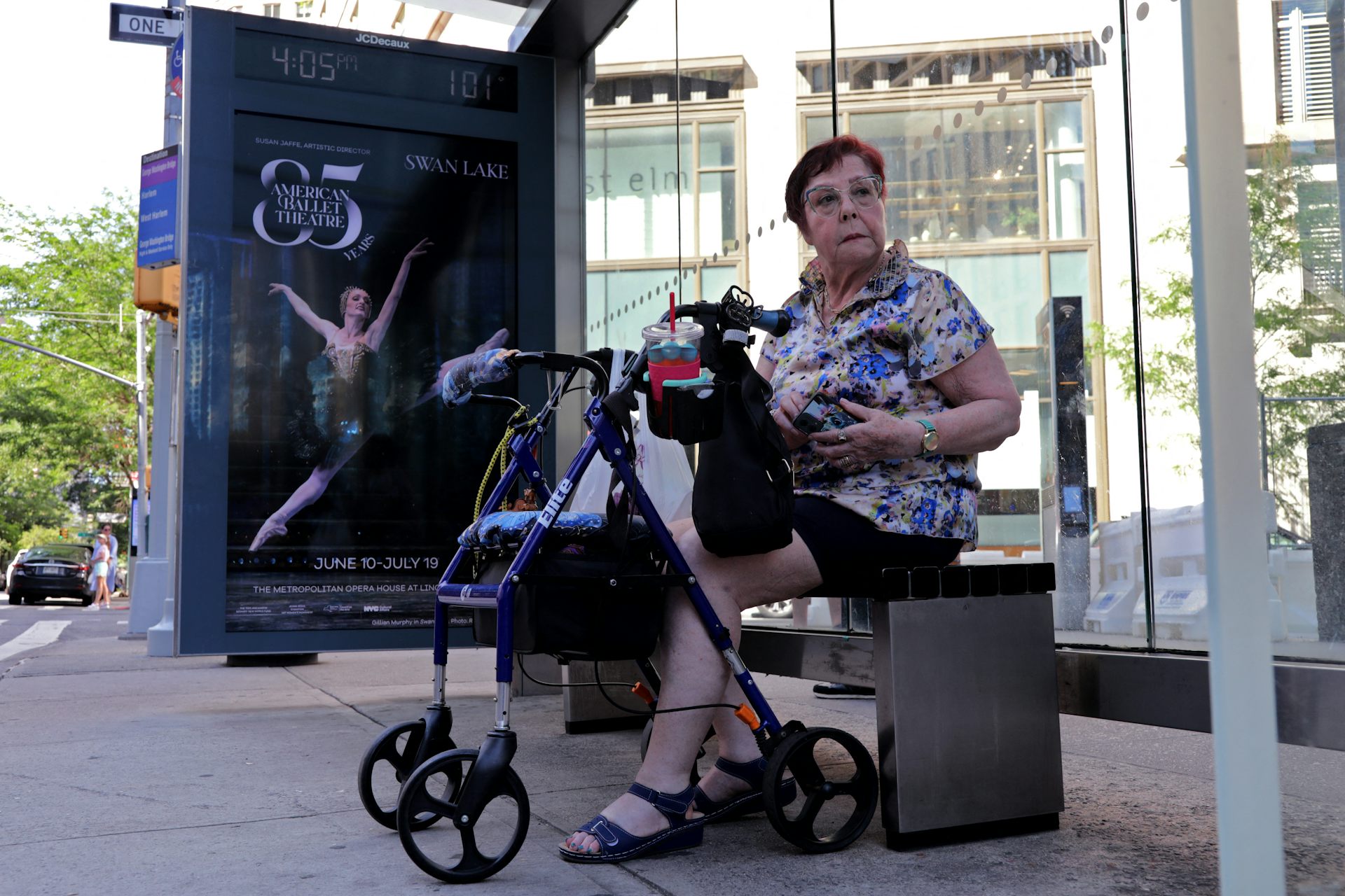 Woman with walker sits on bench under a bus shelter