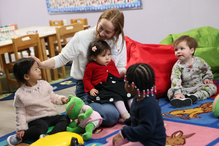A woman sits on a colorful rug with four small children.