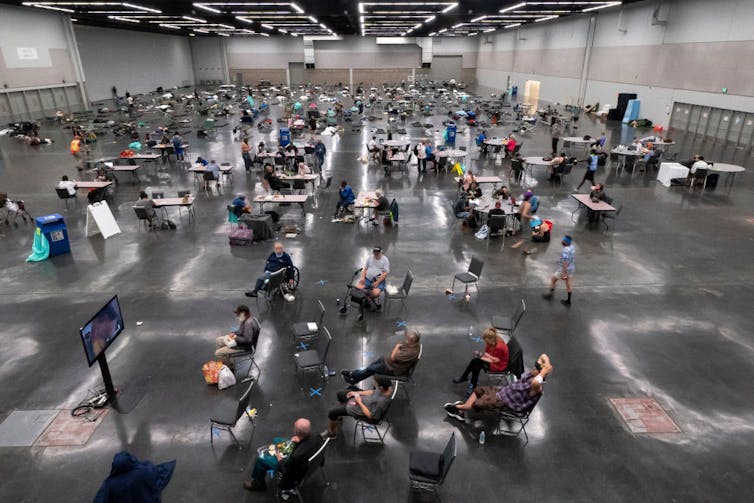 People sitting at chairs and tables spread out in a large warehouse-like room