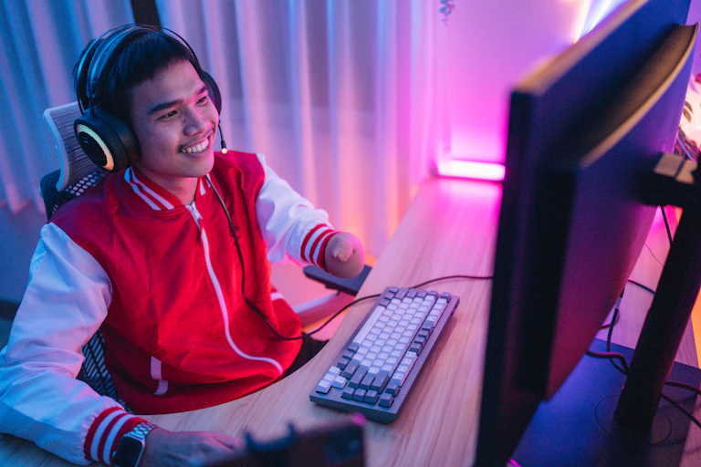 A young disabled man, smiling, wearing headphones playing a computer game.