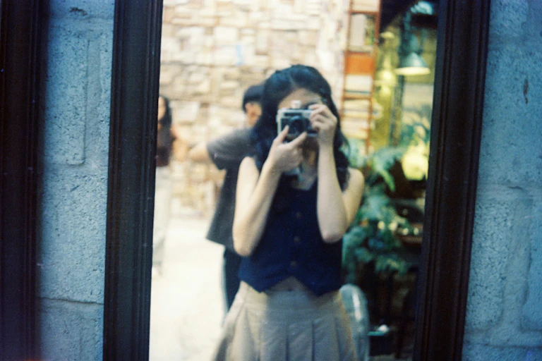 A woman taking a selfie in a mirror with a vintage film camera.
