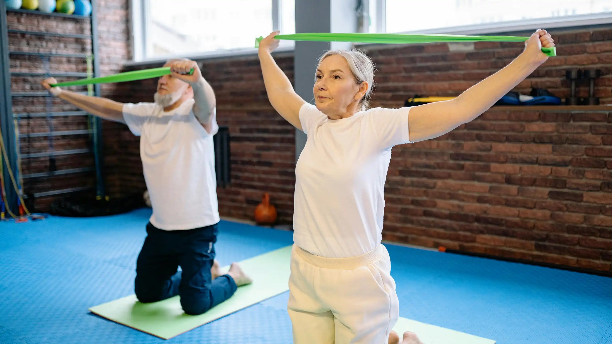 A man and a woman with grey hair using green resistance bands