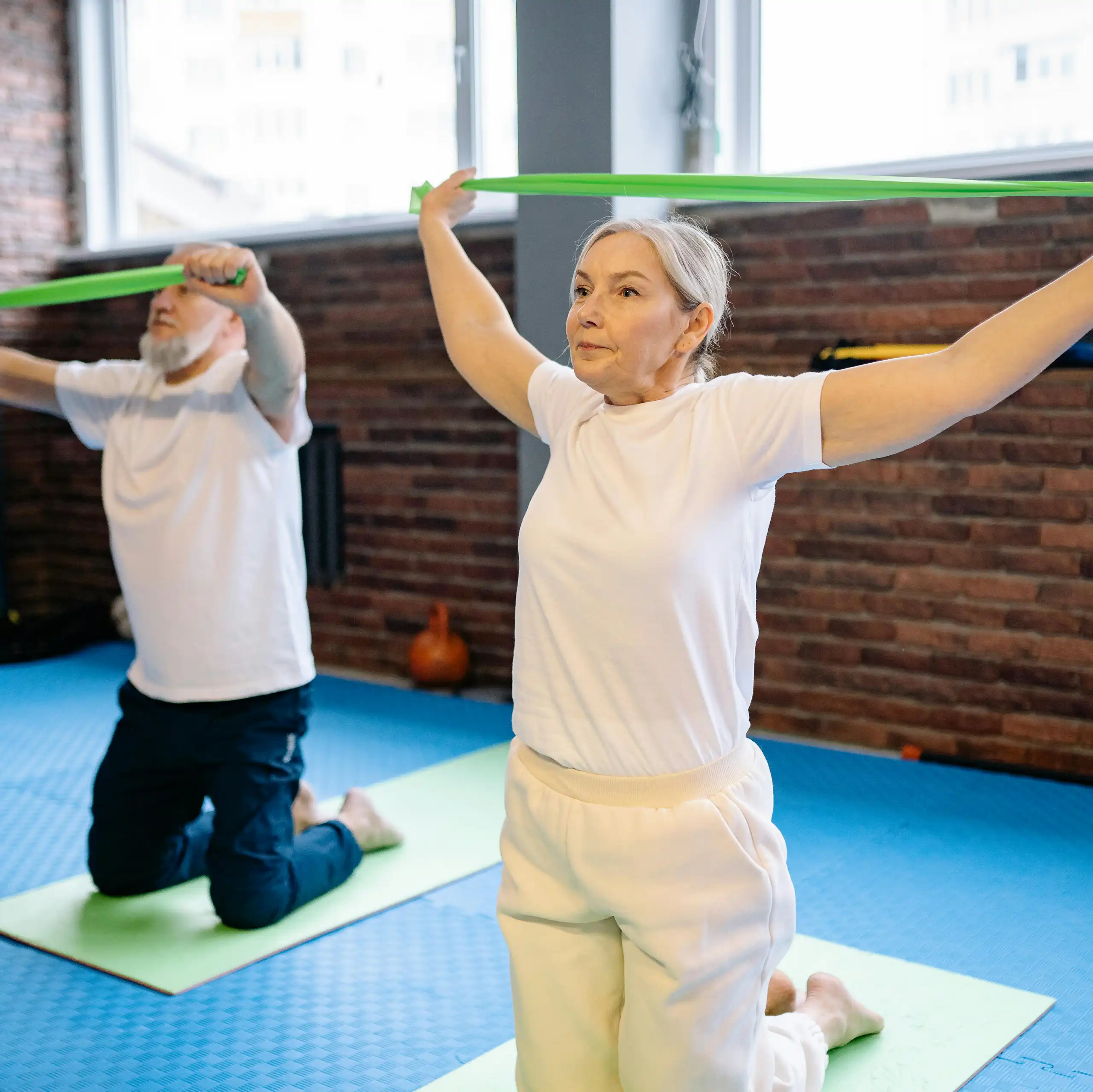A man and a woman with grey hair using green resistance bands