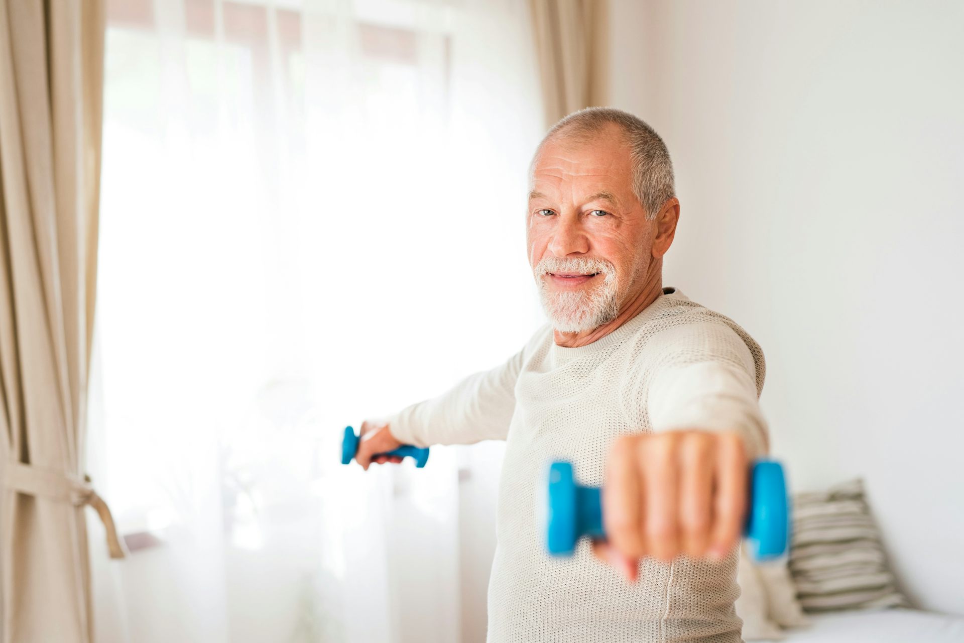 A man with grey hair using two small blue dumbbells