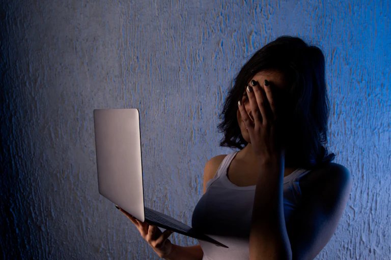 Young woman with her hand over her eyes and her laptop in her hand.