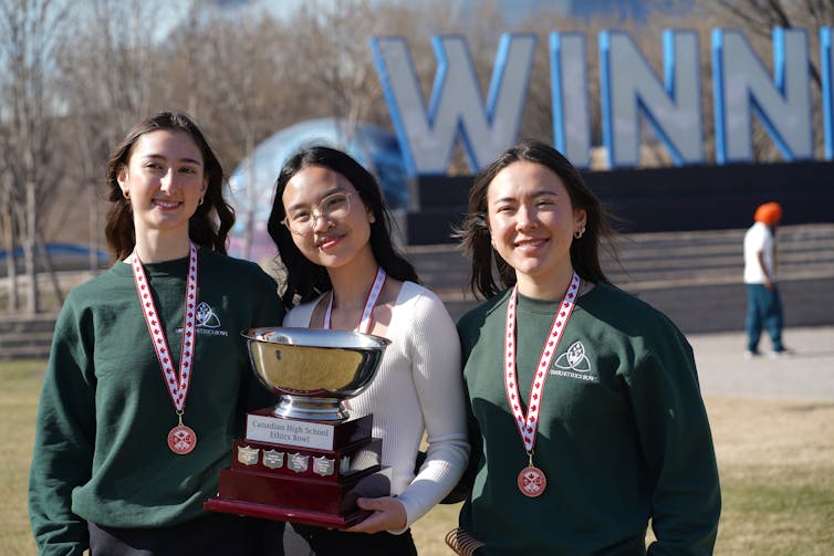 Tres mujeres sostienen el trofeo al aire libre con cuentas alrededor del cuello.