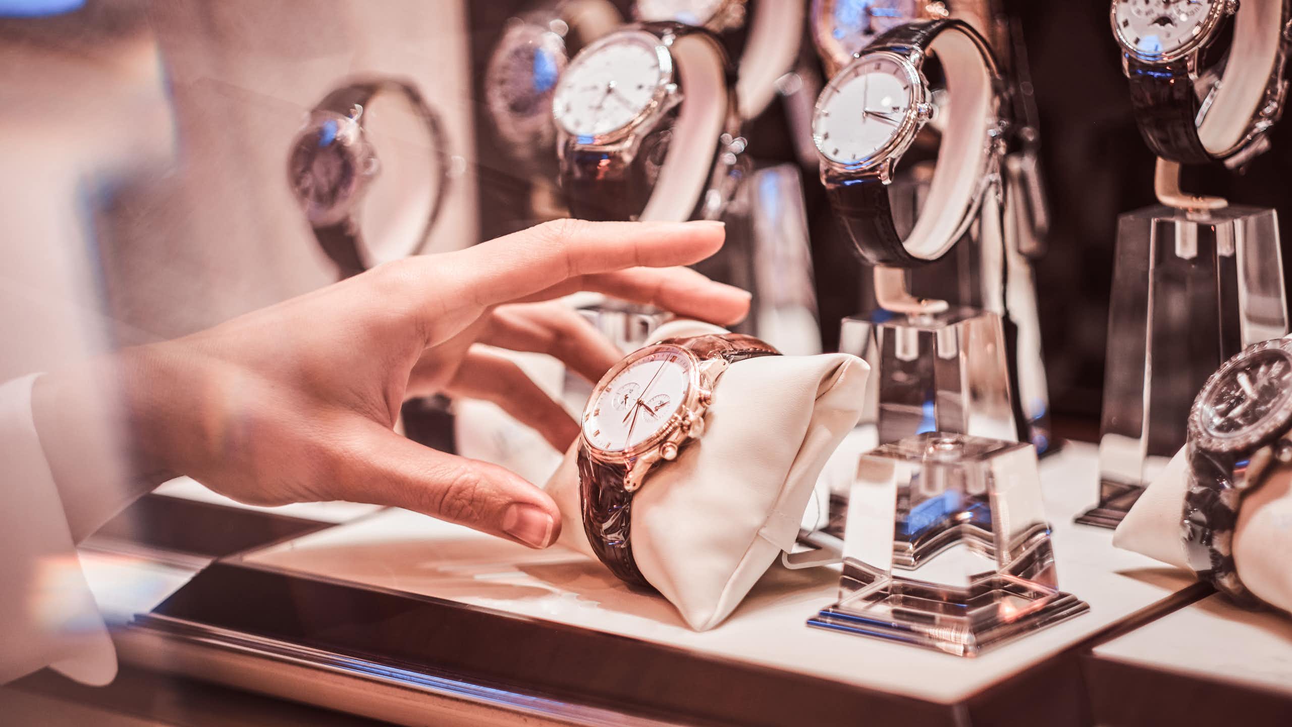 luxury watches on display in a shop window with a hand reaching out to take one.