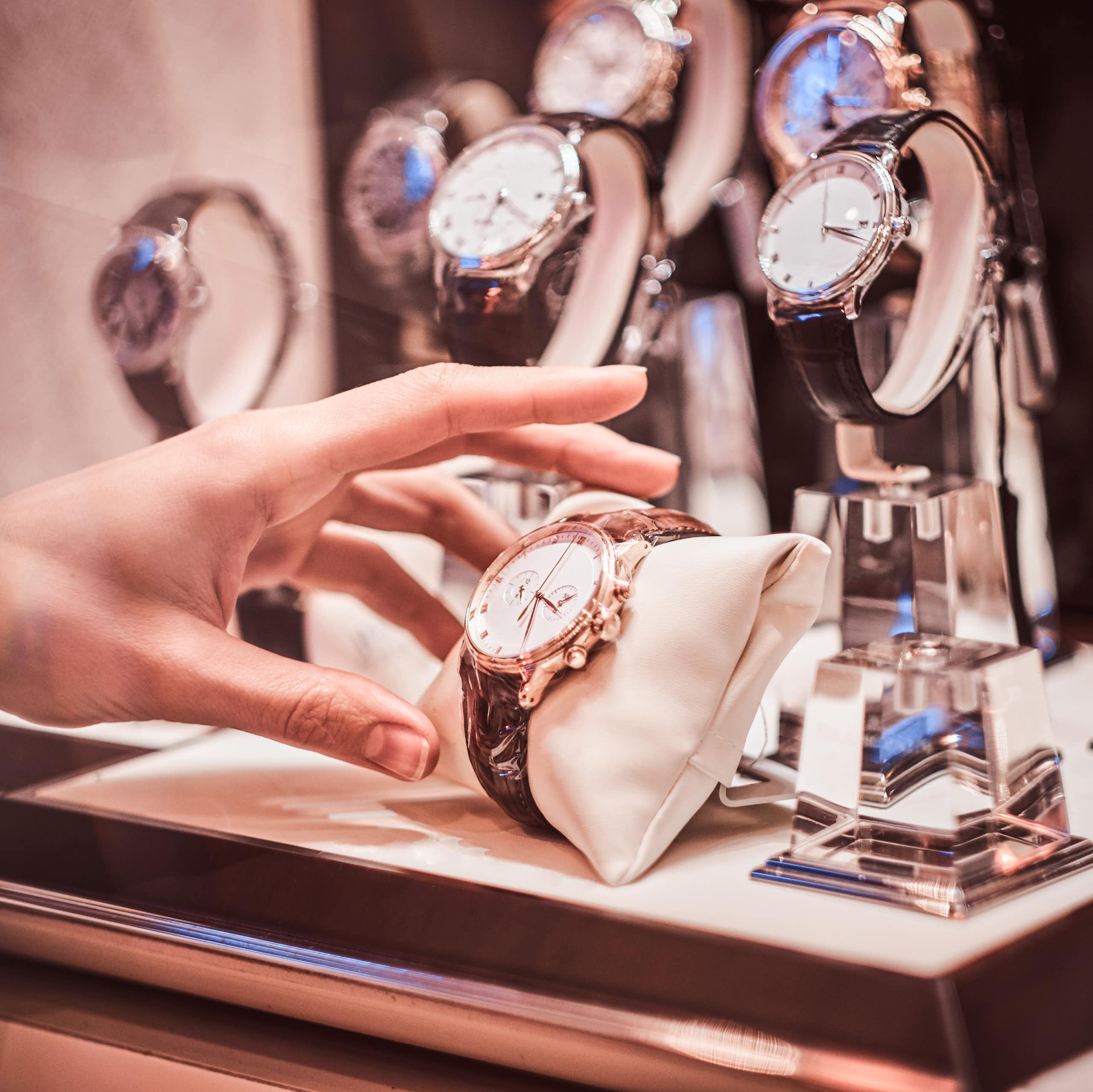 luxury watches on display in a shop window with a hand reaching out to take one.