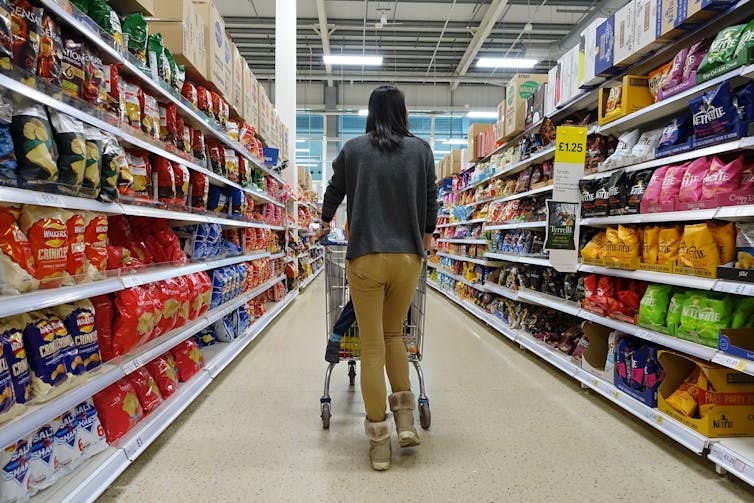 woman pushes a shopping trolley with a child in the seat down a supermarket aisle.
