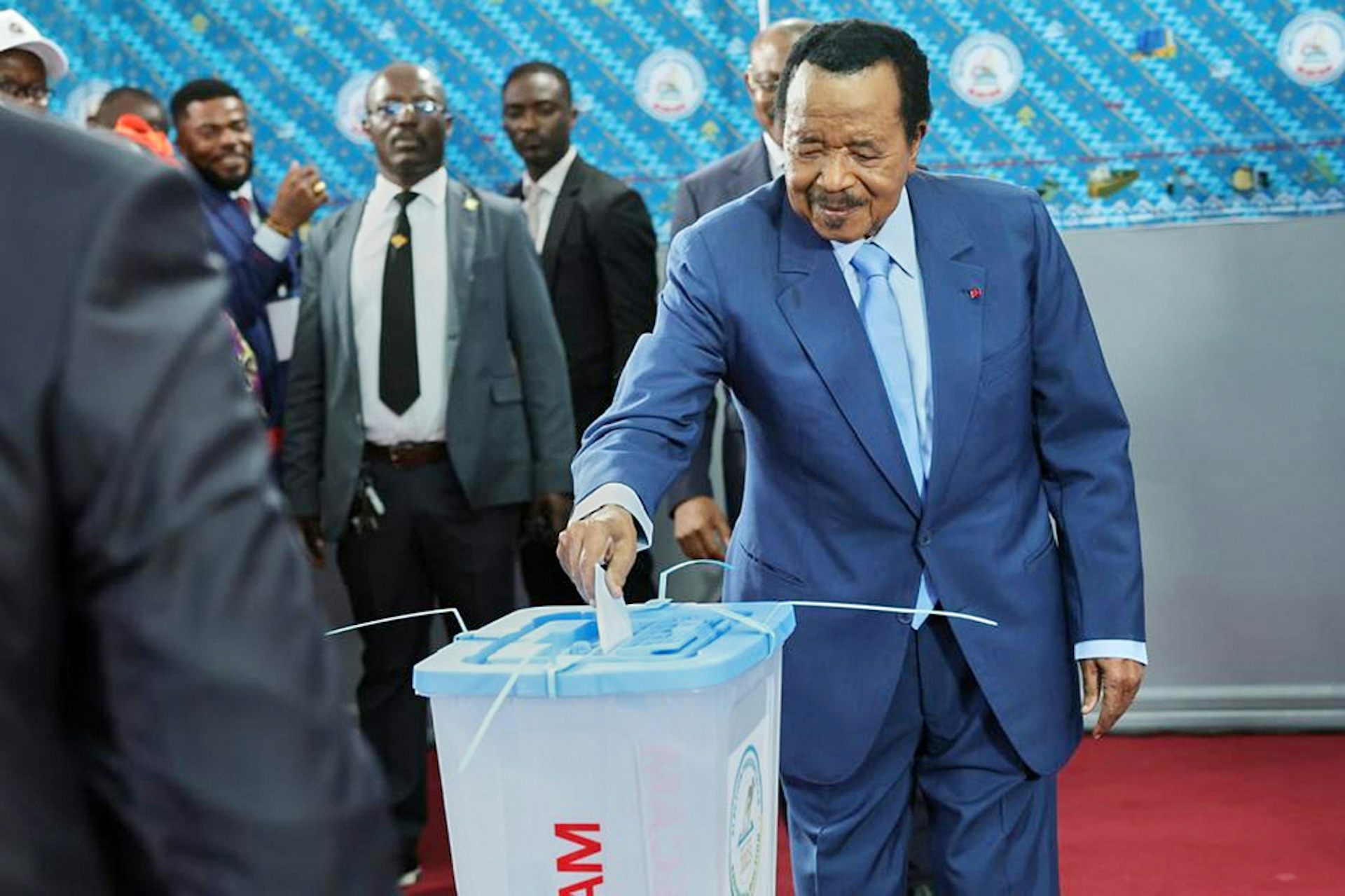 An elderly man in a suit drops his vote into a bin during an election.