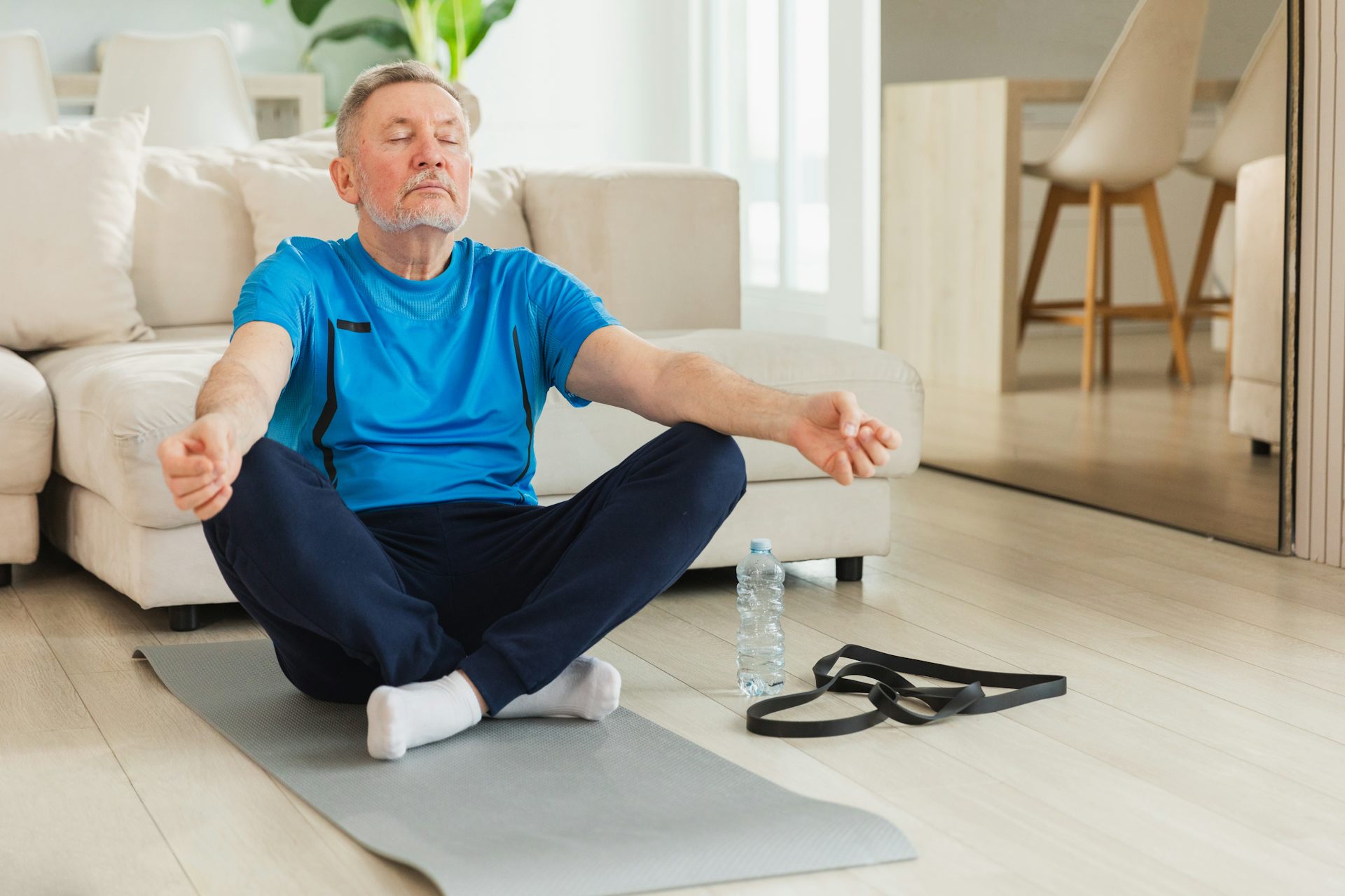 Un monsieur d'un certain âge est assis en position de yoga dans son salon.