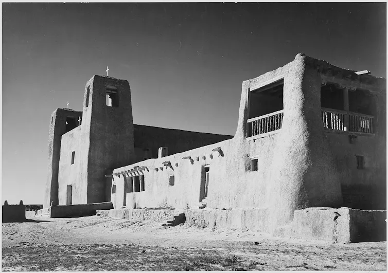 A black and white photograph of a large adobe building with towers.