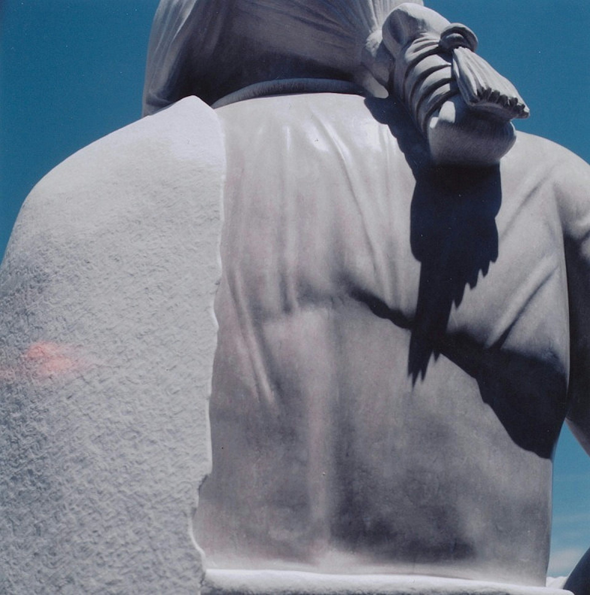 A stone statue of a man with a ponytail and a blanket thrown over one shoulder, seen from the back.