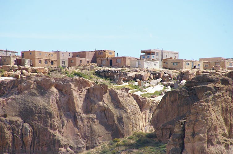 A photo shows a rocky mesa with a cluster of stone or adobe homes on top.