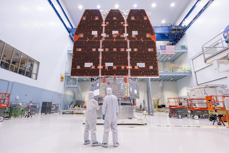 Two engineers in a clean room wearing protective suits looking at the mirror of the assembled Roman space telescope