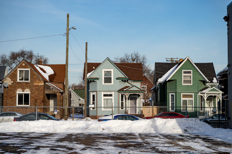 Three neat homes are lined up on a snowy street.