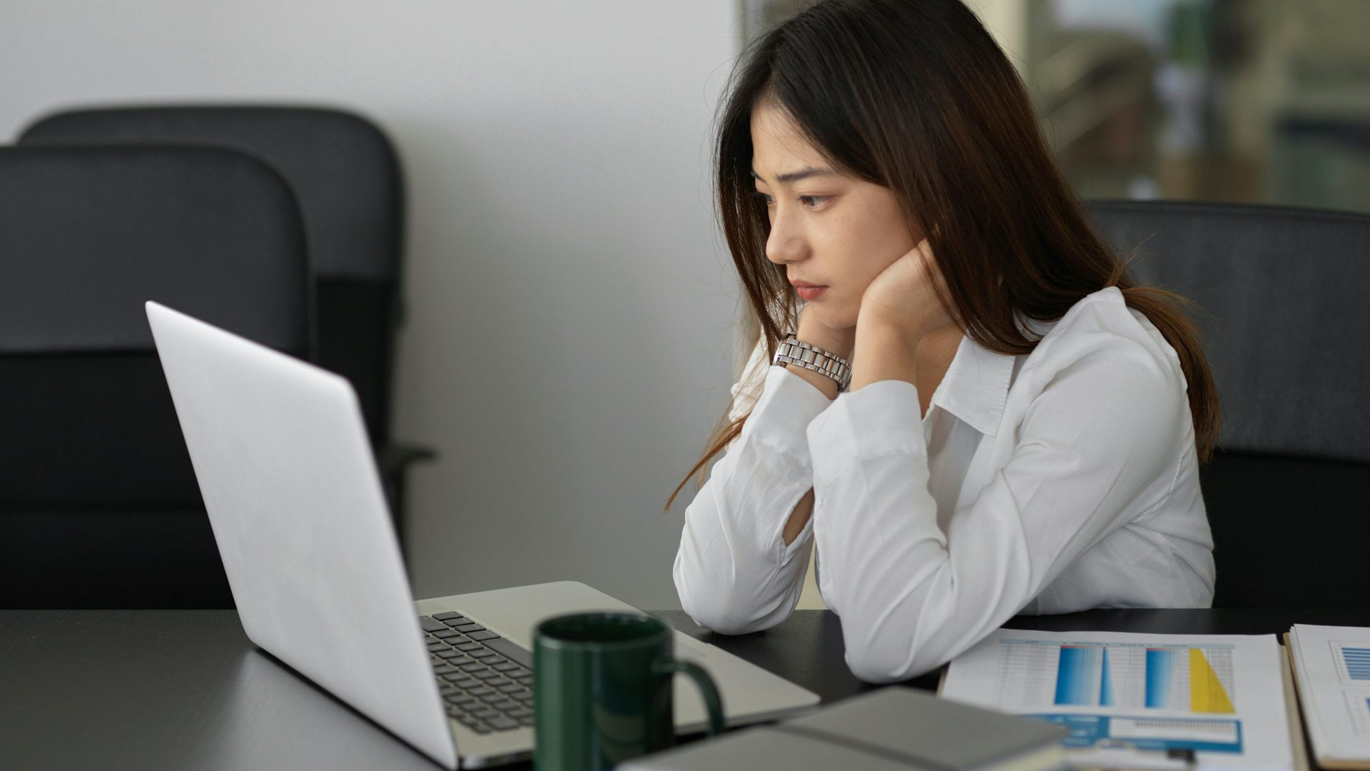 A woman sitting in front of an open laptop looking apprehensive