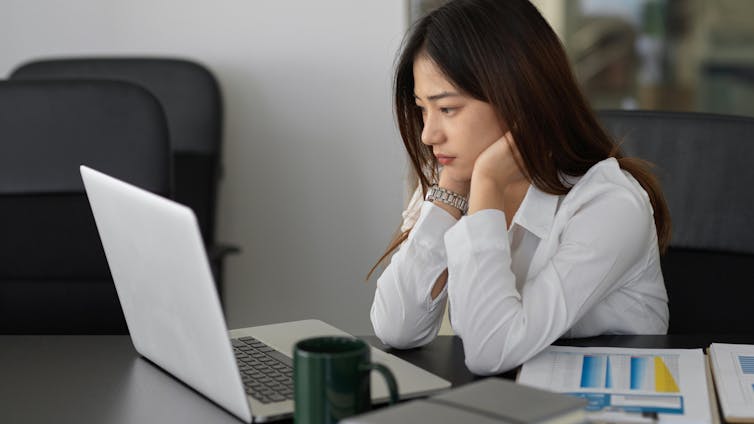 A woman sitting in front of an open laptop looking apprehensive